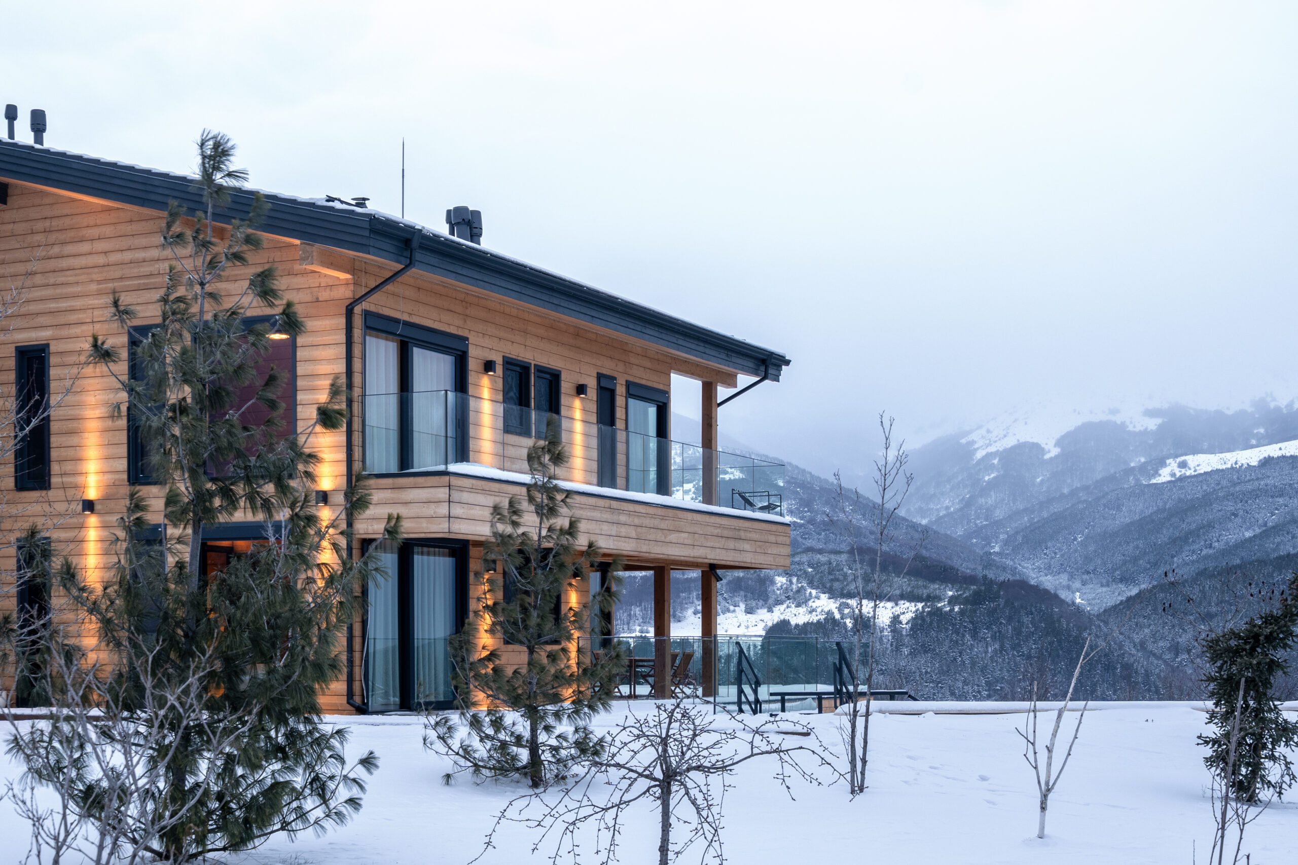 The residence seen from the side, with pine trees and the mountain ridge beyond