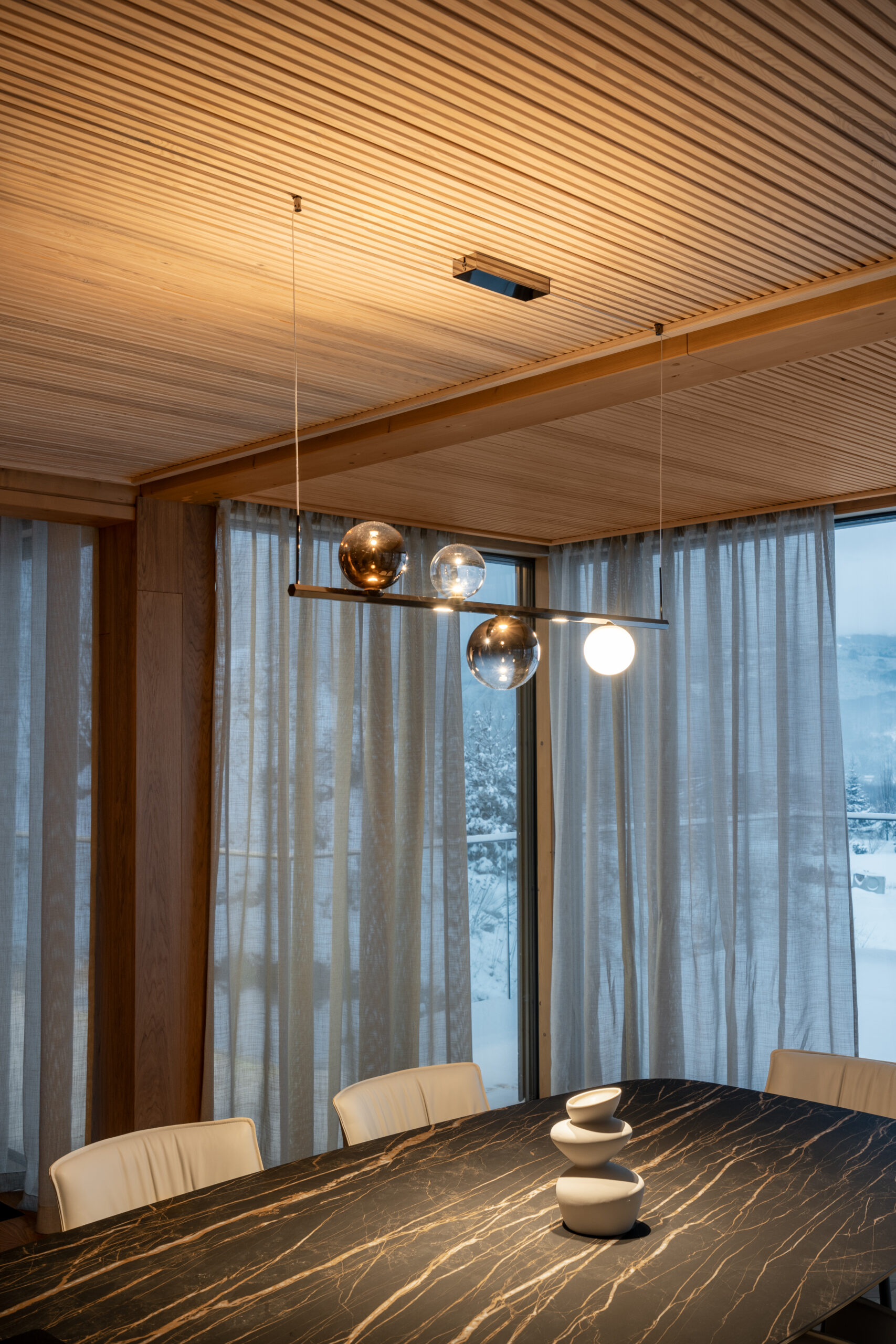 Dining area beneath a timber ceiling, opening towards the snow-covered garden